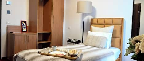 A hotel room with a bed, a bedside table, a lamp, a wardrobe, and a tray with breakfast items.