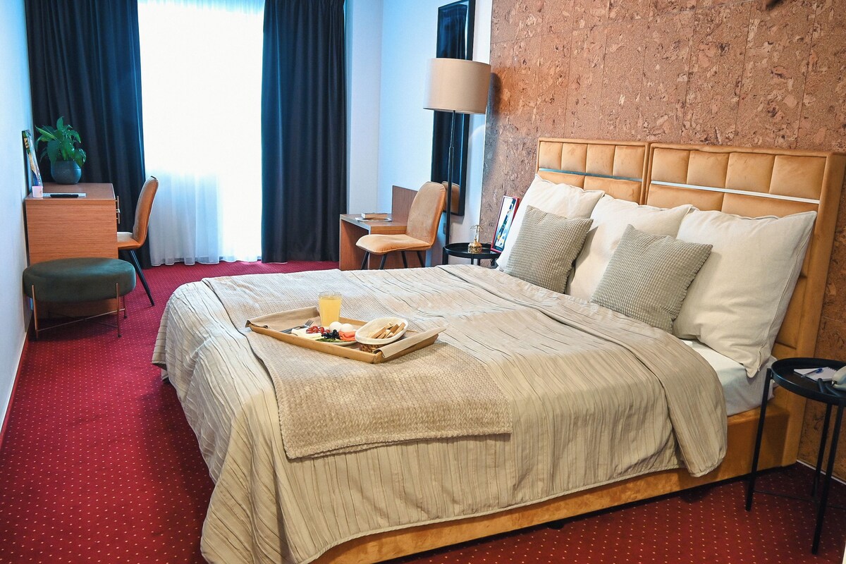 A hotel room with a bed, a desk, a chair, a small table, and a tray with breakfast items.
