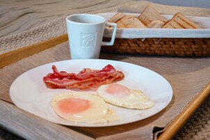 Bandeja de desayuno con tocino y huevos, una taza blanca y una cesta de tostadas.
