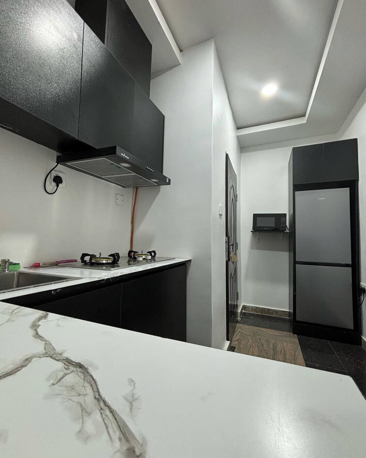 A modern kitchen with black cabinets, a white marble countertop, a built-in stove, and a microwave on a shelf.