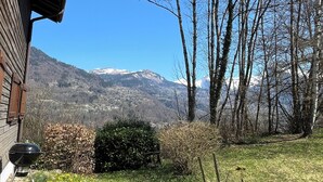 A view of a mountain landscape with a wooden building and a grassy area with yellow flowers.