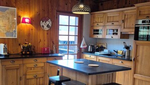 A spacious kitchen with wooden cabinets, a large island with stools, and a hanging pendant light.