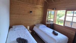 A cabin with two beds, wooden walls, and a window with a view of greenery.