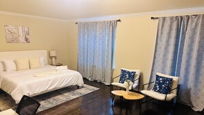 Quarto de hotel com uma cama grande, duas poltronas, uma mesinha e uma escrivaninha.