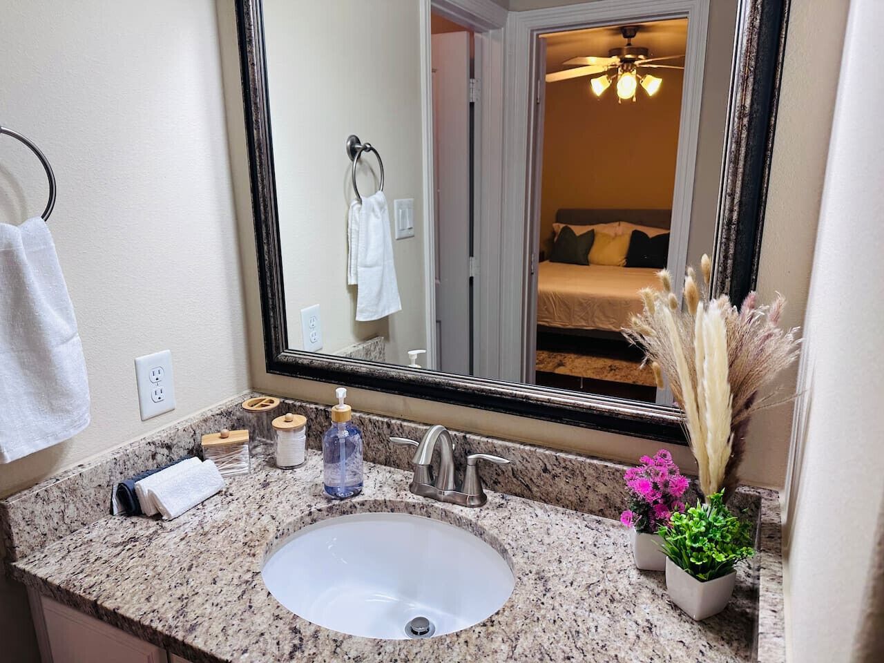 Une salle de bain avec un comptoir en granit, un lavabo blanc, un miroir et une plante en pot.