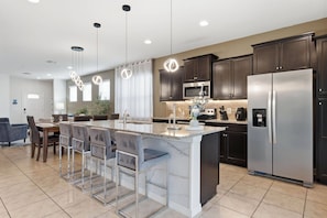A modern kitchen with dark wood cabinets, stainless steel appliances, and a marble island with bar stools. - Fantastic 5 BD Pool home@ Windsor at Westside 9021 (Kissimmee)