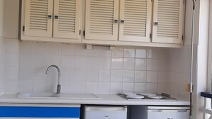 Una cocina con armarios blancos, un fregadero, un refrigerador pequeño y una zona de comedor con una mesa y sillas.