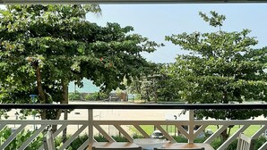 Un patio cubierto con una mesa y sillas, barandilla y vista a árboles y un edificio al fondo.