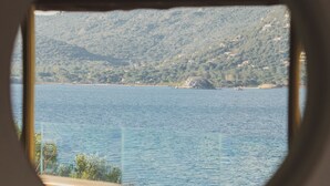 A view through a circular window of a body of water, a distant shoreline, and a hilly landscape. - Luxury Villa with private beach and splendid pool on Sea Front (Porto-Vecchio)