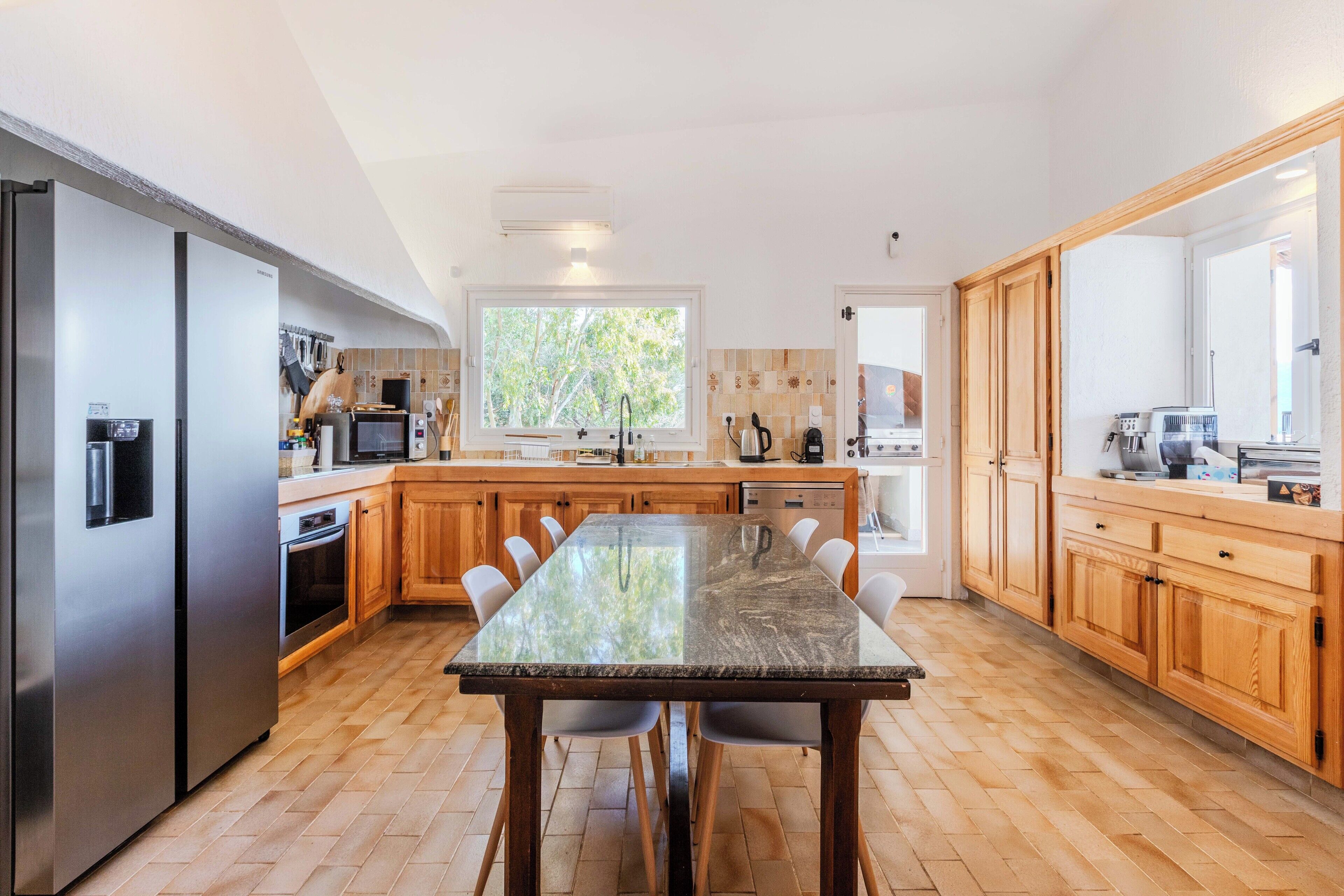 A modern kitchen with a central island, stainless steel appliances, wooden cabinets, and a large window providing natural light.