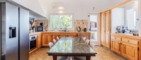 A modern kitchen with a central island, stainless steel appliances, wooden cabinets, and a large window providing natural light.