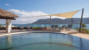 A swimming pool with lounge chairs and a shaded area, overlooking a mountainous landscape. - Luxury Villa with private beach and splendid pool on Sea Front (Porto-Vecchio)