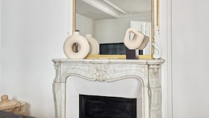 Un camino bianco con decorazioni elaborate, uno specchio con cornice dorata sopra e due vasi color crema sulla mensola.