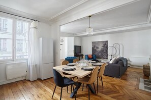 Un soggiorno moderno con zona pranzo, caratterizzato da un pavimento a spina di pesce, un divano grigio e un grande quadro astratto appeso alla parete.