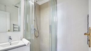 Un bagno moderno con doccia vetrata, lavandino bianco e asciugamano sul mobile.