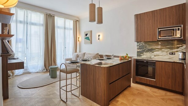 A modern kitchen with wooden cabinets, a built-in microwave, and a marble countertop.