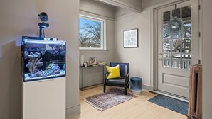 A room with a large aquarium, a chair with a yellow cushion, a framed picture on the wall, and a door with a wreath. - This 2 bedroom 2 bathroom elegantly furnished home is ready for all your needs.  Featuring a primary bedroom suite, TV room, dining room, and additional sitting areas. (Chicago)