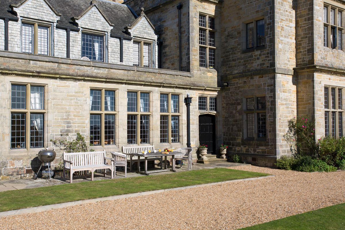 A stone building with a patio area featuring a table and chairs, a barbecue grill, and a well-maintained lawn.