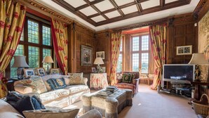 A traditional living room with wooden paneling, a large sofa set, a television, and a fireplace.