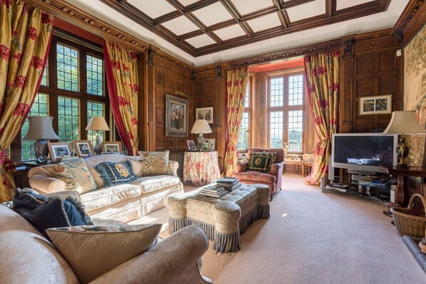 A traditional living room with wooden paneling, a large sofa set, a television, and a fireplace.