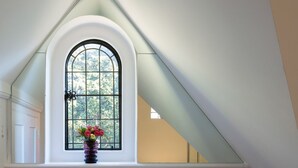 A room with a large arched window, a vase with flowers, and a sloped ceiling.