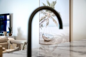 Ein modernes Wohnzimmer mit großem Fenster, einem Hängekorbstuhl mit Blick auf den Strand und einem Fernseher auf der linken Seite.