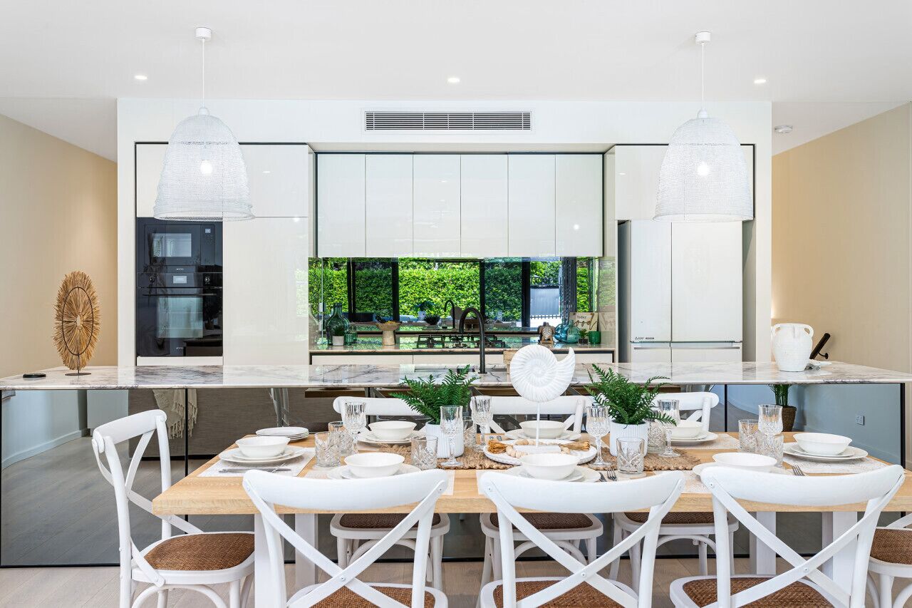 A modern kitchen with white cabinetry, a large island with seating, pendant lighting, and a view of greenery outside.