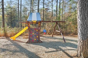 A playground with a climbing wall, a slide, and a swing set in a wooded area. - Private Resort Retreat: Pool, Sauna, Golf + Pond (Broken Bow)