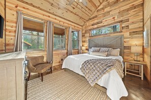 A wooden cabin bedroom with a bed, a chair, and a nightstand. - Private Resort Retreat: Pool, Sauna, Golf + Pond (Broken Bow)