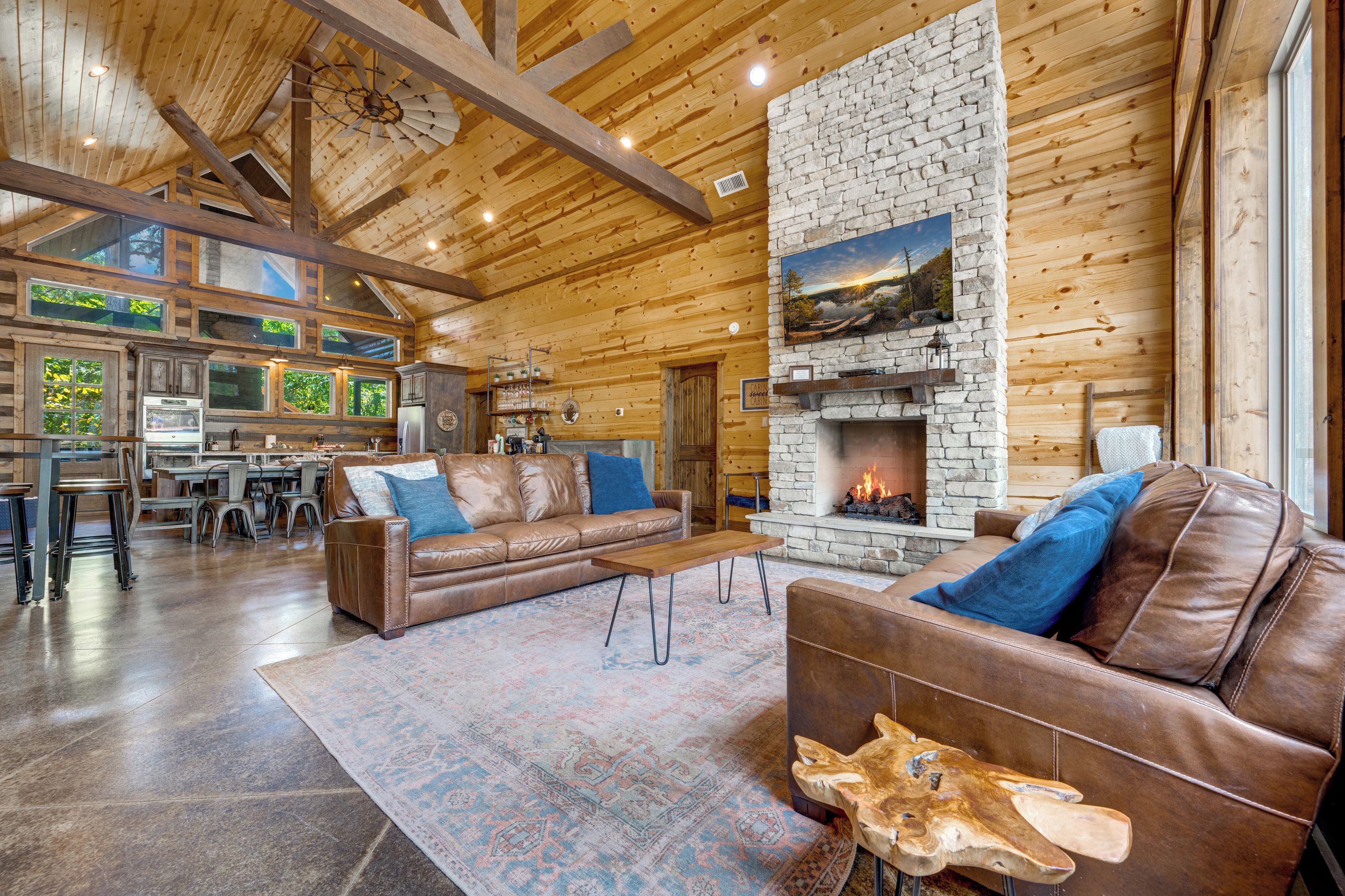 Uma sala de estar ampla, com lareira de pedra, sofás de couro e um tapete grande.