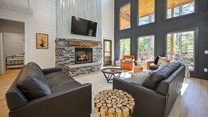 Un salon moderne doté d’une cheminée en pierre, de canapés en cuir et de grandes fenêtres offrant une vue sur l’extérieur.