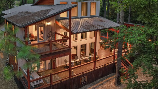 Une cabane en bois à deux étages, dotée d’un balcon et d’une terrasse couverte, entourée d’arbres.