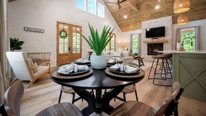 Una sala de estar moderna con chimenea, techo de madera y un comedor con una mesa redonda y sillas.