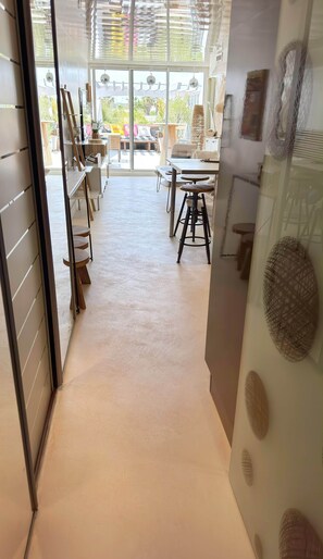 A hallway leading to a dining area with a view of the outdoors, a seating area with a table and chairs, and a decorative wall with woven patterns.