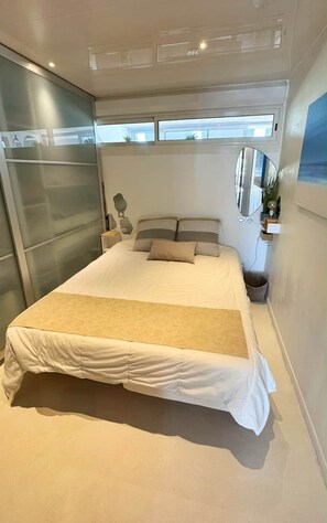 Ein modernes Schlafzimmer mit einem großen Bett, einem Nachttisch, einem Spiegel und Blick ins Freie.