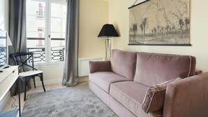 A living room with a beige sofa, a desk with a chair, a lamp, and a map on the wall. - Apartement Center of Paris (Paris)