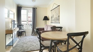 A dining area with a round table, four chairs, a sofa, a lamp, and a window with curtains. - Apartement Center of Paris (Paris)