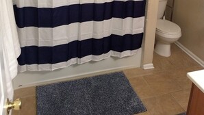 A bathroom with a striped shower curtain, a toilet, and a small rug.