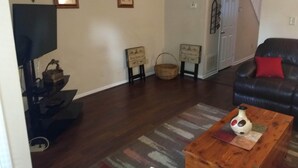 A living room with a dark leather sofa, a wooden coffee table, a television, and framed pictures on the wall.