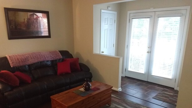 A living room with a black leather sofa, a wooden coffee table, a patterned rug, and a door with a window.