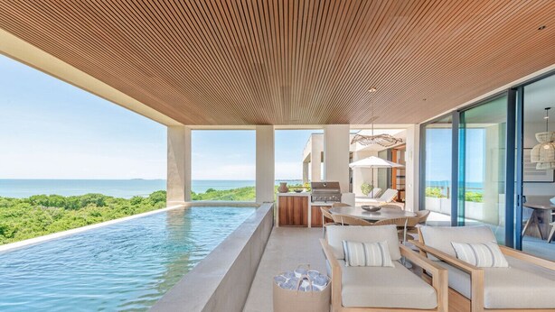 Un espacio exterior moderno con piscina, mobiliario de madera y vistas al océano.