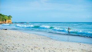 Una playa con un surfista caminando por la orilla, olas rompiendo y un cielo despejado.