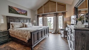 Un dormitorio con una cama grande, cabecera de madera, ventilador de techo, cómoda y una ventana con cortinas.