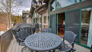 Una terraza con una mesa redonda y sillas, una parrilla cubierta y un ventanal corredizo que da a un espacio interior.