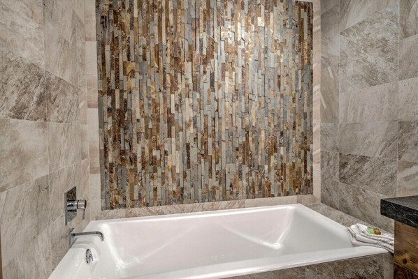Un baño moderno con una bañera rectangular, un muro de mosaico y suelo de mármol.