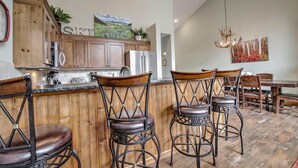 Una cocina con armarios de madera, una zona de bar con taburetes y una mesa de comedor con sillas.