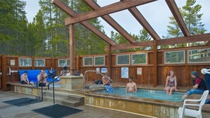 Una piscina exterior de madera con techo cubierto, rodeada de árboles.