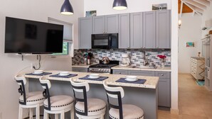 Une cuisine moderne avec des meubles gris, un micro-ondes noir, un grand téléviseur et un coin bar avec des tabourets.