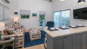 Une cuisine moderne dotée d’un îlot central, un coin repas agrémenté d’un tapis bleu et un espace détente avec des poufs à motifs.