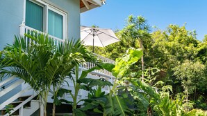 Une maison dotée d’un balcon, entourée d’une végétation luxuriante et abritée par un grand parasol.